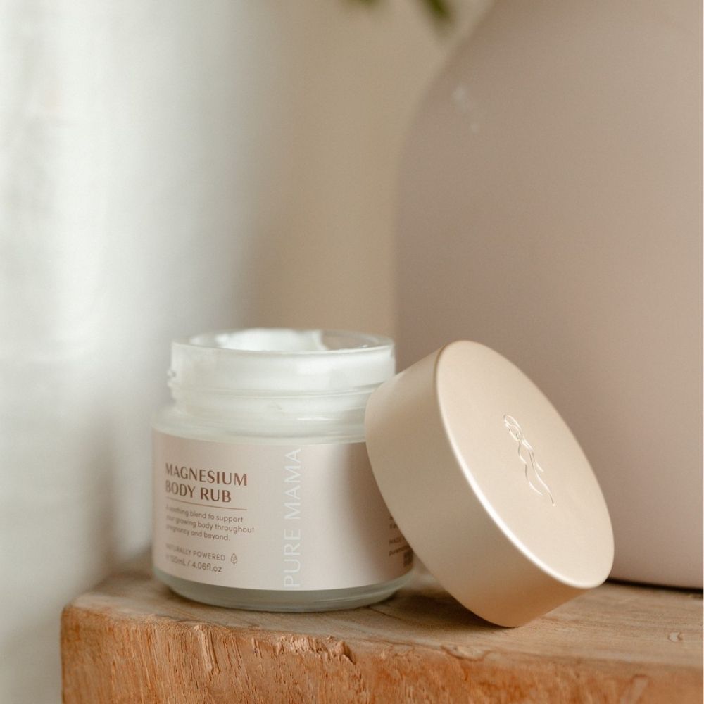 A jar of Pure Mama Magnesium Body Rub rests on a wooden surface, its minimalist packaging adding a calming touch—ideal for soothing pain relief and relaxation.